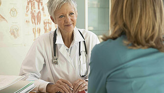 Frau spricht sitzend mit Ärztin