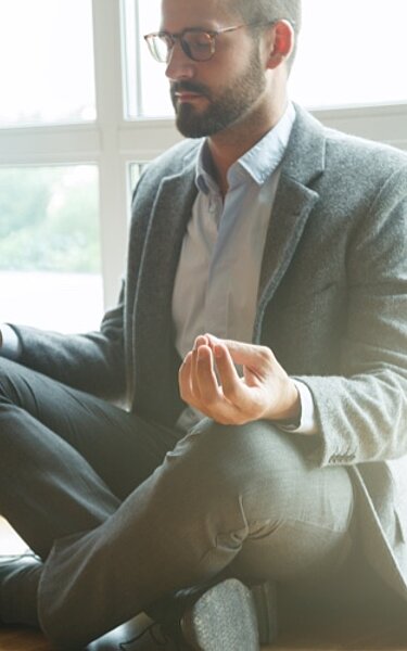 Ein Mann im Anzug gönnt sich im Büro eine Pause im Yoga-Sitz.