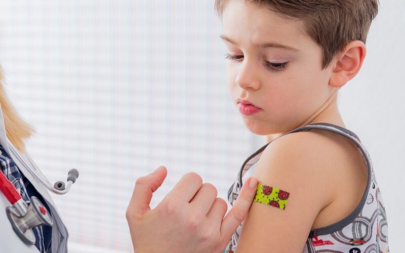 Ein kleiner Junge bekommt nach dem Impfen ein buntes Pflaster auf den Arm geklebt.