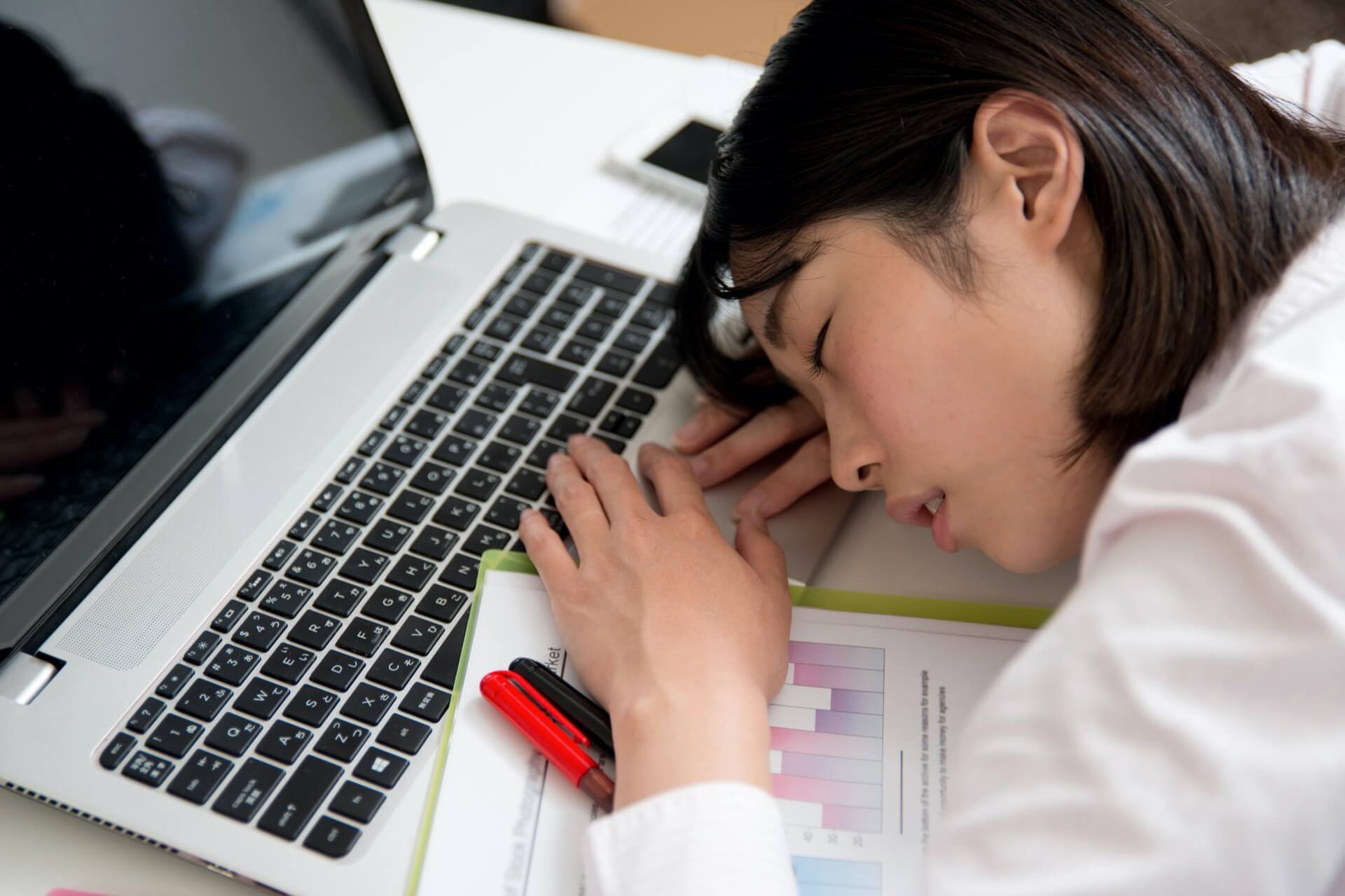 Müde asiatische Geschäftsfrau liegt schlafend auf einem Notebook