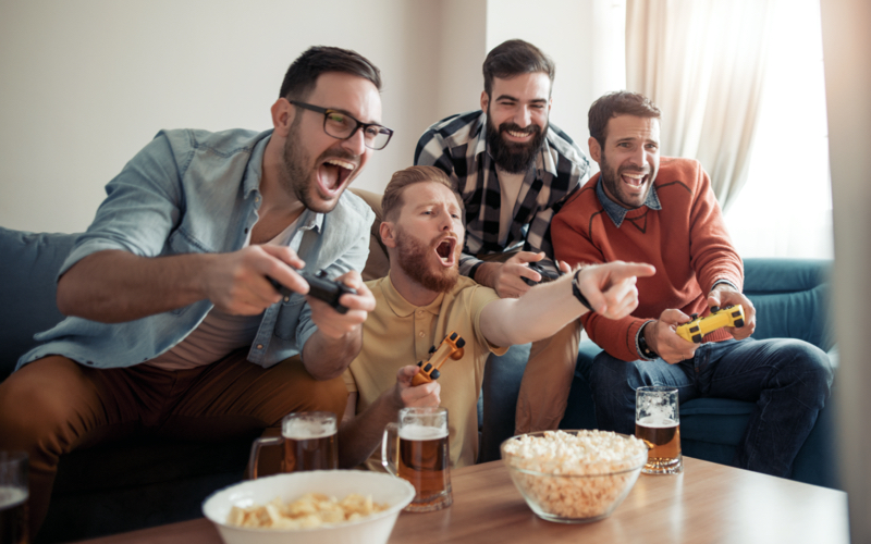 Vier junge Männer treffen sich mit Bier und Popcorn zum Video-Spielen.